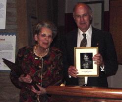 Barbara Mueller looks on as Chairman Roger Brody holds the photograph to be placed on the USSS Hall of Fame wall at the American Philatelic Center.